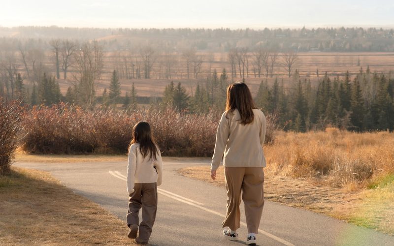 A parent and child walking together outdoors at golden hour.