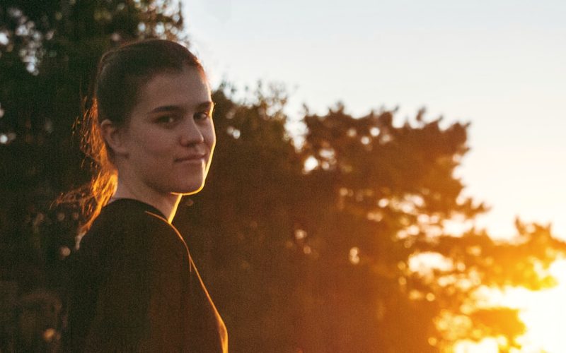 A young woman outdoors in warm evening light.